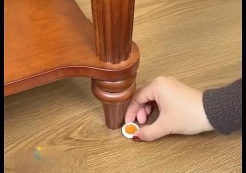 Hand applying a small container of glue to a wooden table leg.